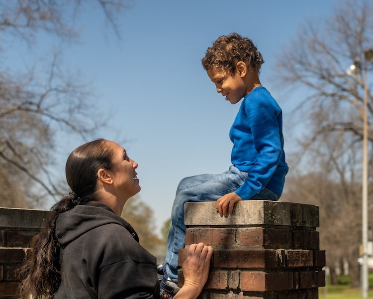 Un niño sentado sobre ladrillos mirando a su mamá